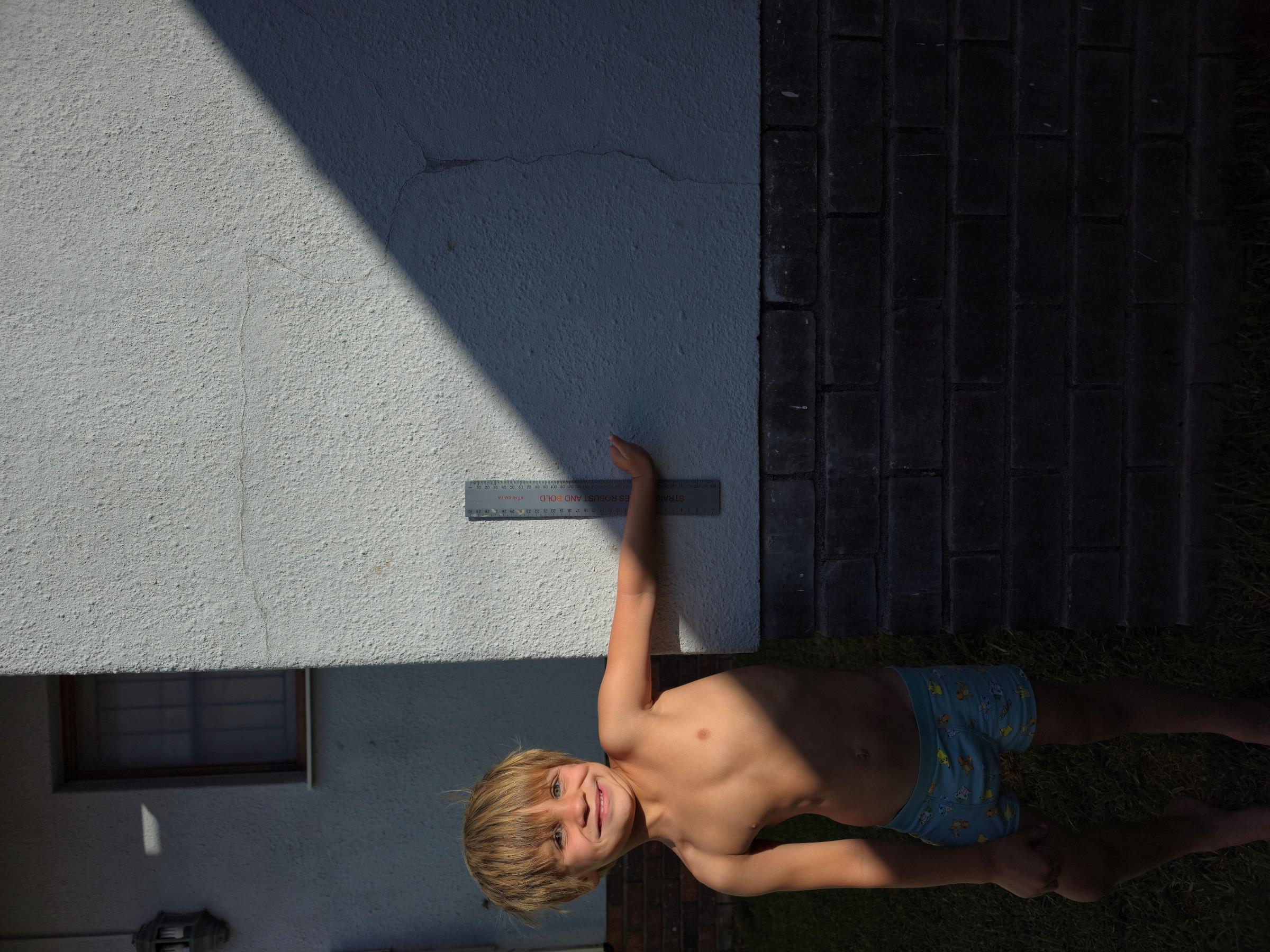 Noah smiling outside with his left arm extended toward the camera, measurement photo